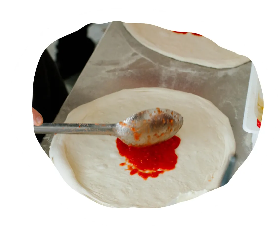 Spreading tomato sauce on a pizza base